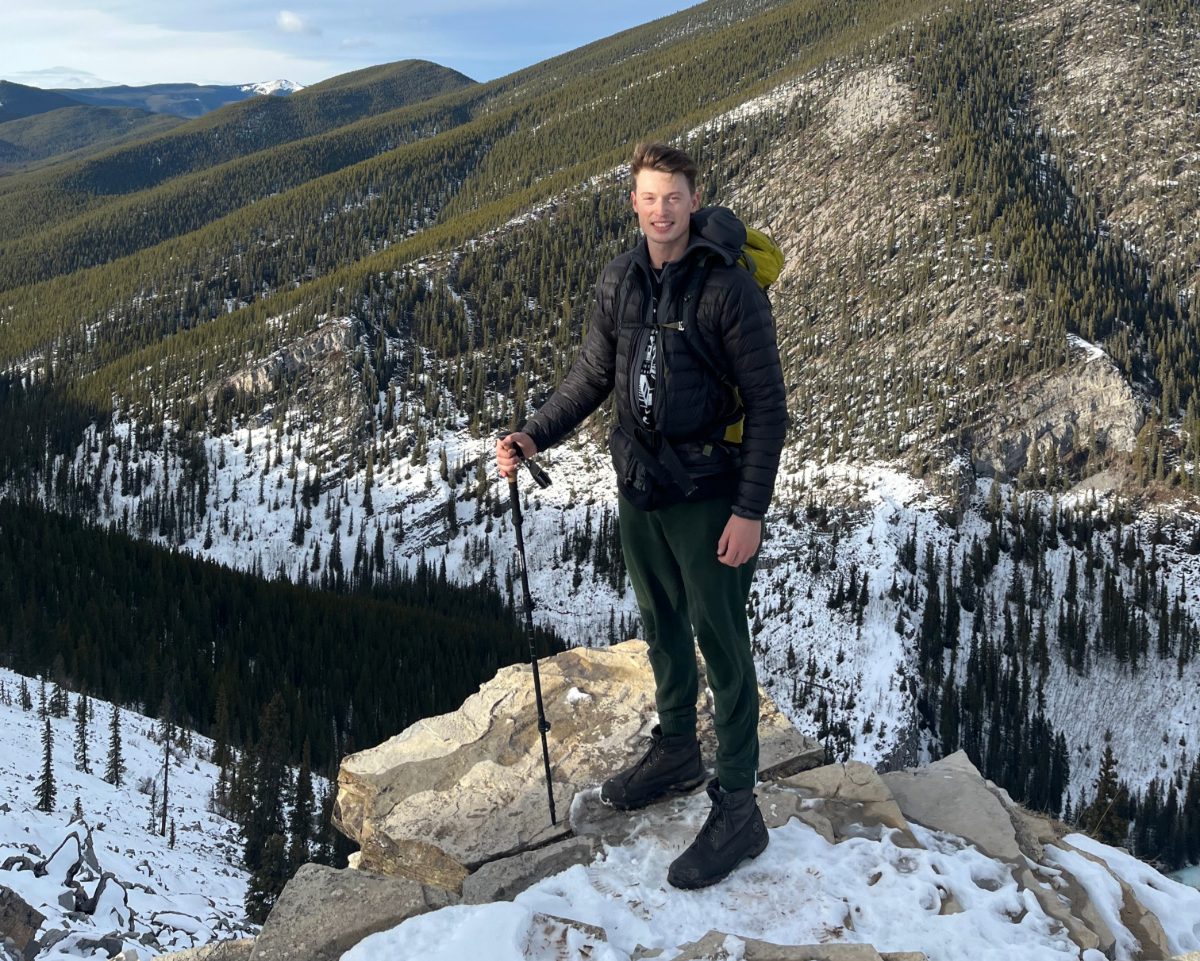 William Mai standing atop a mountain with some snow cover in hiking gear in Alberta.