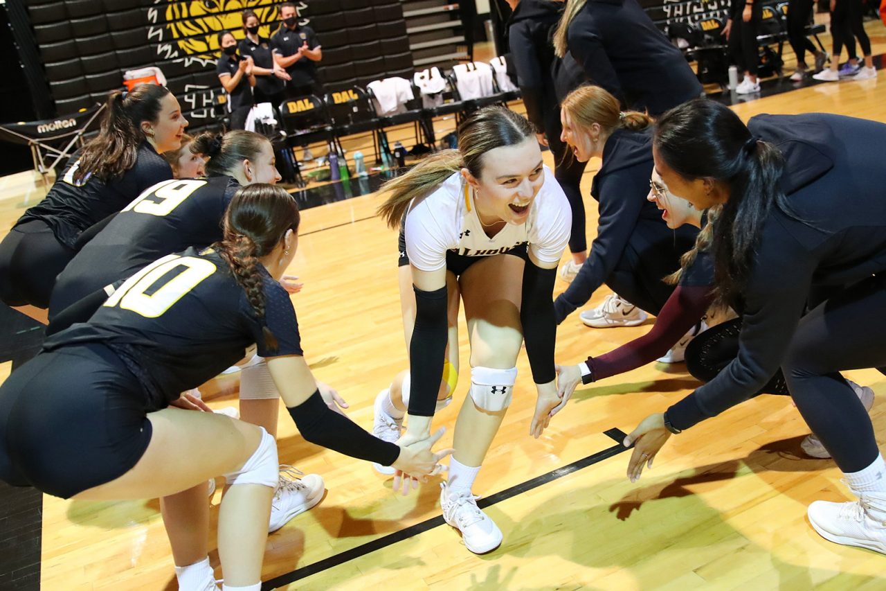 Women's volleyball team dressed in black and gold uniforms giving each other high fives.