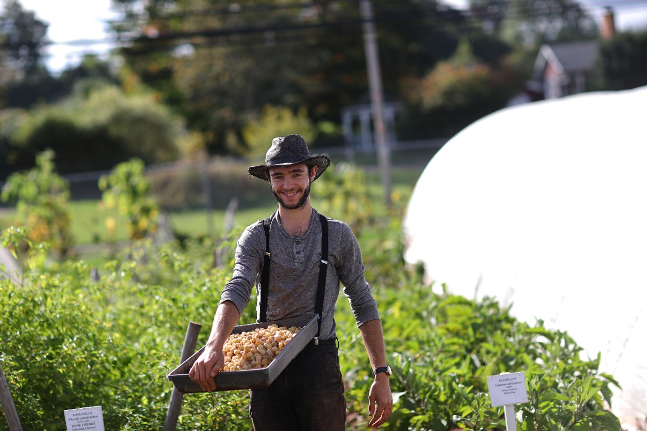Student standing in field holding a tray of vegetables.