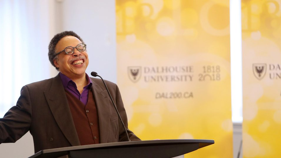 George Elliott Clarke recites the Bicentennial Poem while standing at a podium in front of a gold Dalhousie sign. 