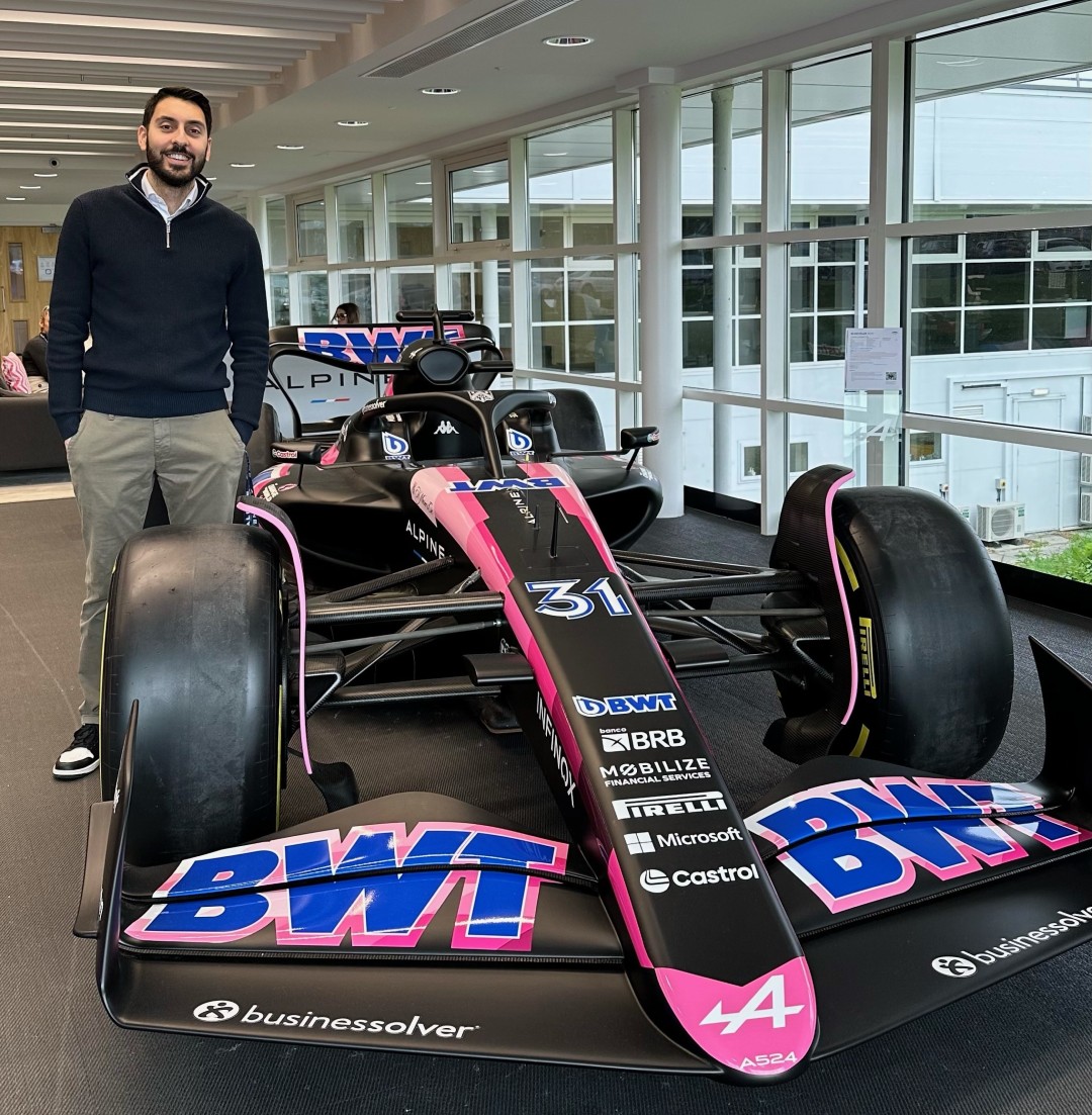 Ahluwalia stands smiling next to a BWT racing vehicle indoors next to a wall of windows.