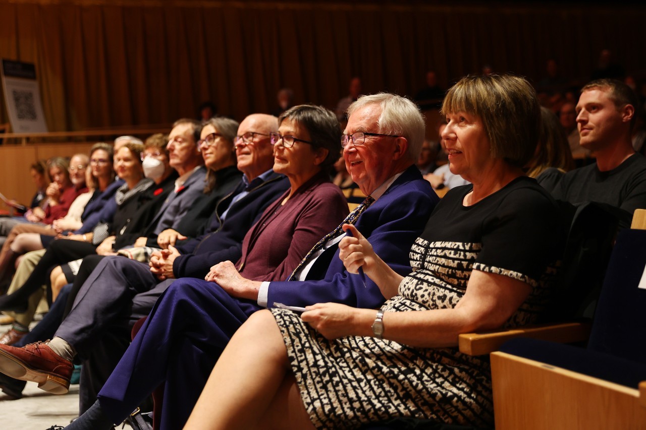 A group of people in suits and dresses sit in the seats of an auditorium