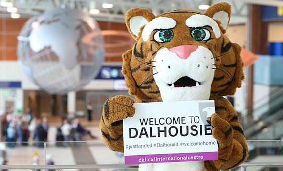 Dal's tiger mascot holds a sign that says 'Welcome to Dalhousie' outside the arrivals gate at Halifax Stanfield International Airport.
