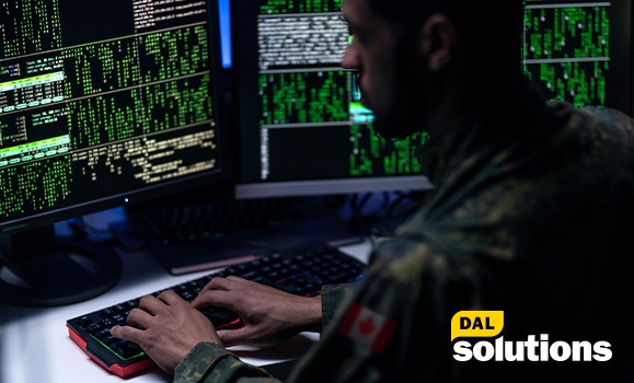 Someone is seen typing on a keyboard with four screens displaying green and white computer coding.