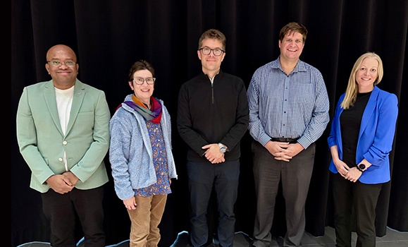 Four panelists stand together in front of a black backdrop.