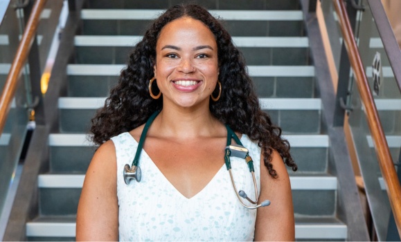 Sierra Sparks is standing in front of a set of stairs with a stethoscope around her neck. 