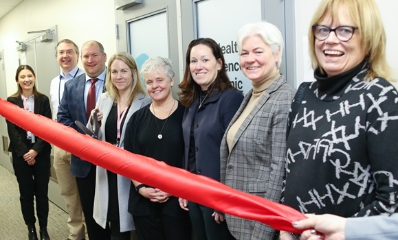 Eight people are seen behind a bright red ribbon that is about to be cut.