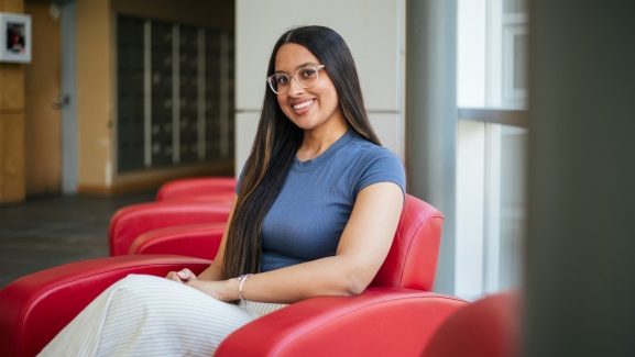 Kaitlin McNeil is sitting seen sitting in a red leather chair smiling at the camera.