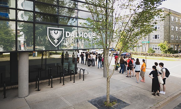 A line of students next to the glass windows of the Mona Campbell Building.