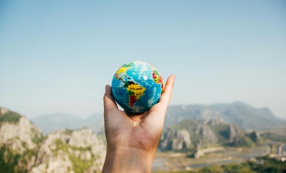 A hand is shown holding a mini globe with mountains in the background.