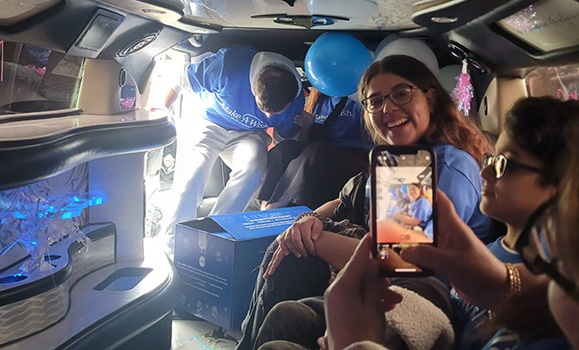 Zeen Ali is smiling in a limo with blue and white balloons.