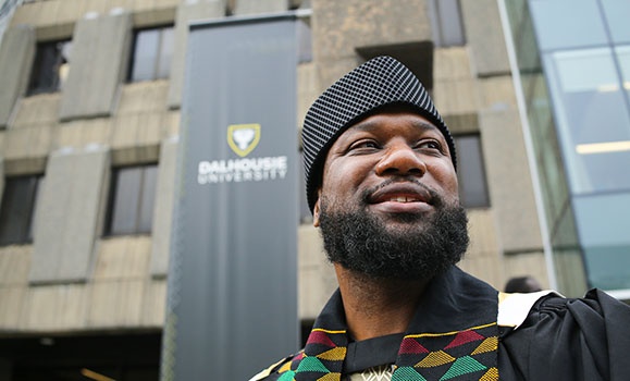 Phillip Jackson is standing in front of a Dalhousie University pull-up banner wearing a Kente sash.