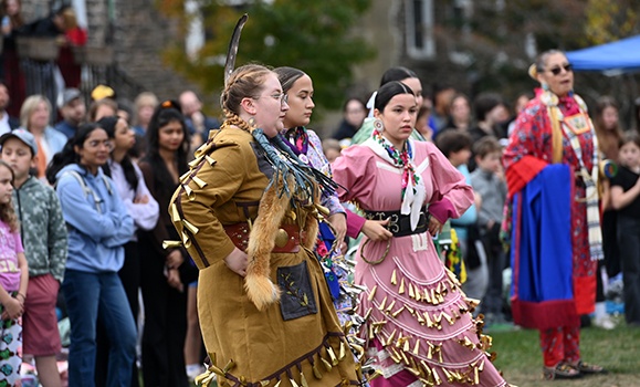 A crowd gathers to watch three dancers in traditional wear.