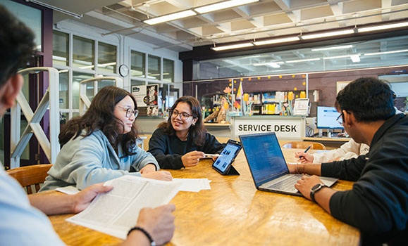 A group of students with their laptops are sitting at a table.