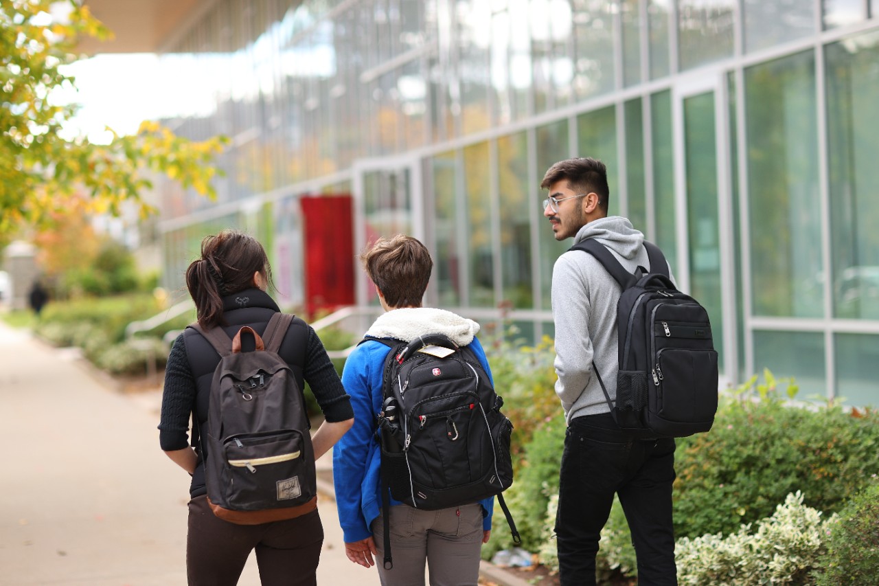 three students with backpacks walking outside