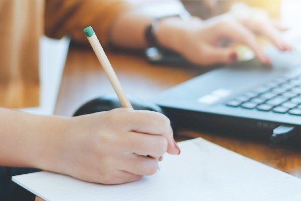 person using laptop and handwriting notes