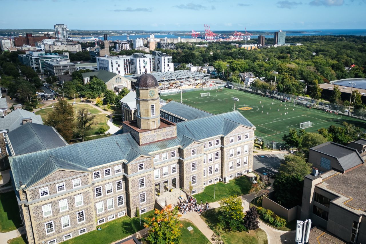 An aerial view of Dalhousie's Studley campus showing the Henry Hicks building and Wickwire field, with Halifax Harbour in the distance.