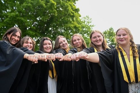 Seven students are standing together holding their hands out to show off their barley rings.