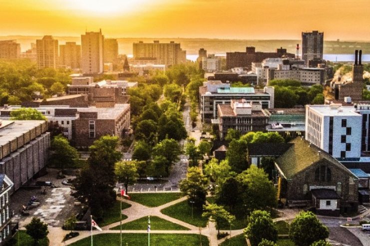 The sun sets on the horizon with Dalhousie's Halifax campus in the foreground and downtown Halifax buildings and Halifax Harbour in background.