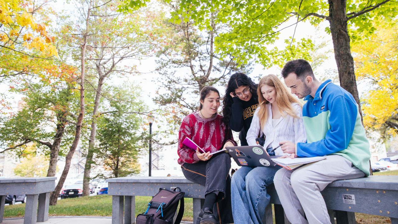 four students outside looking at a laptop