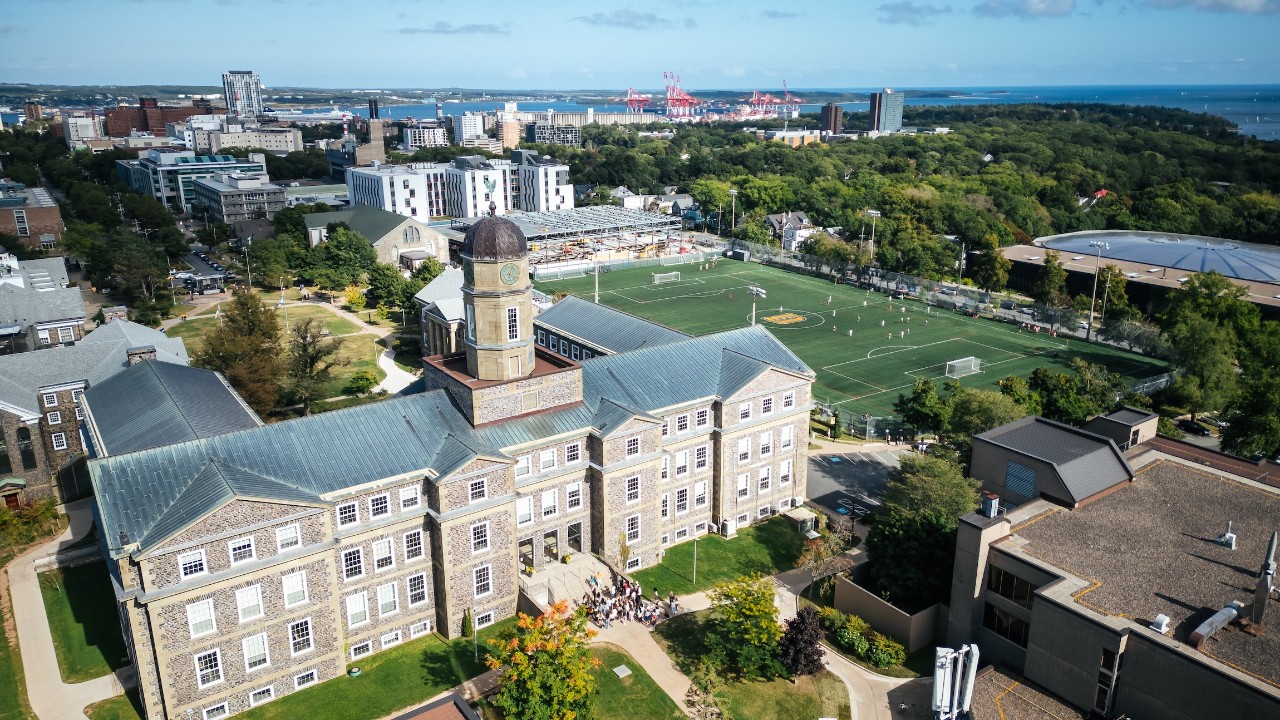 An aerial view of Dalhousie's Studley campus showing the Henry Hicks building and Wickwire field, with Halifax Harbour in the distance.