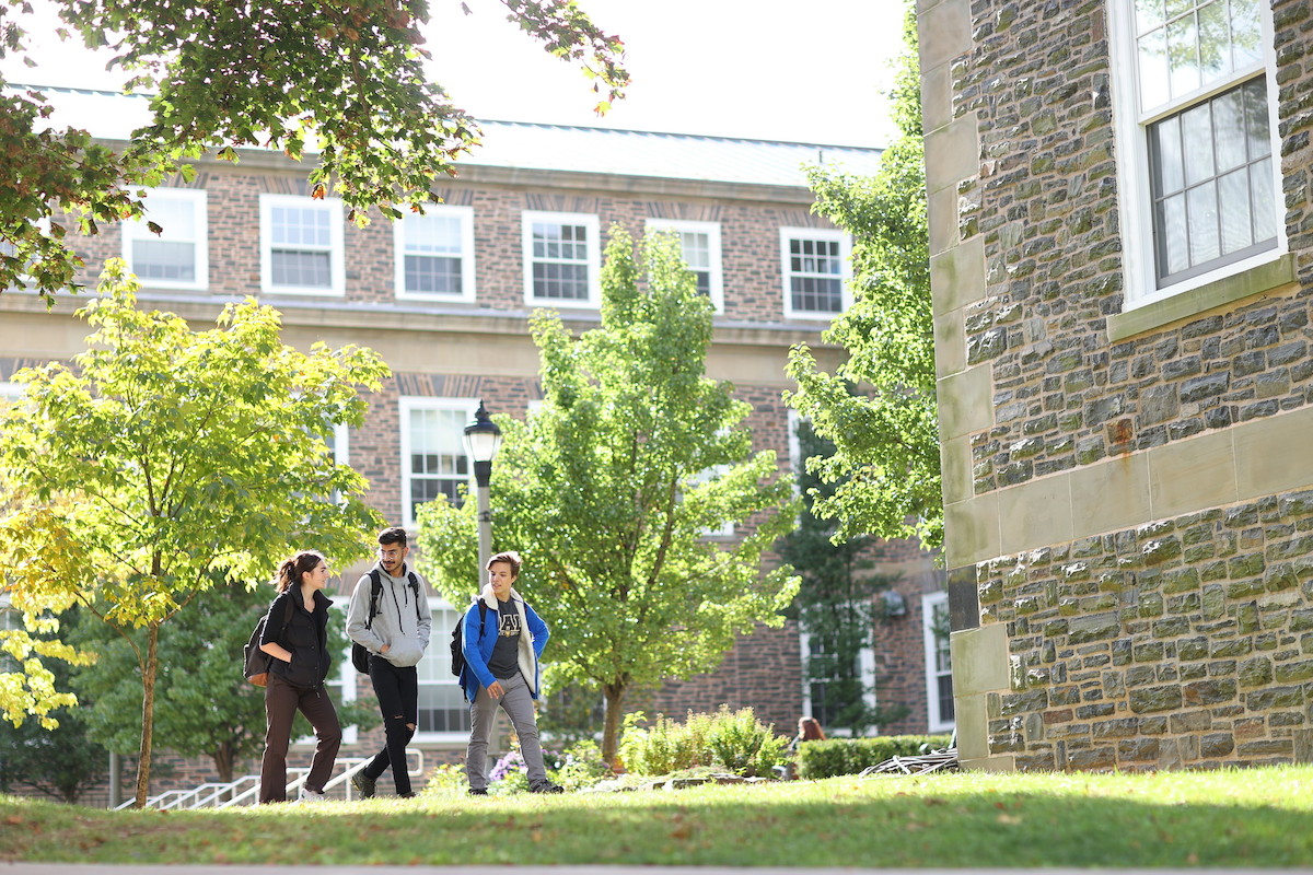Three students walk across the Studley Quad with the Henry Hicks Building in the background.