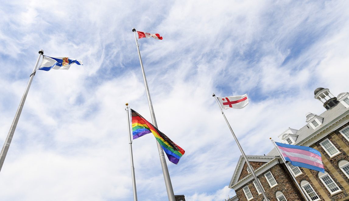 The Nova Scotia, Canadian, Mi'kmaq, pride, and trans flags flying on the Studley Quad. The MacDonald Building can be viewed in the backgroudn.