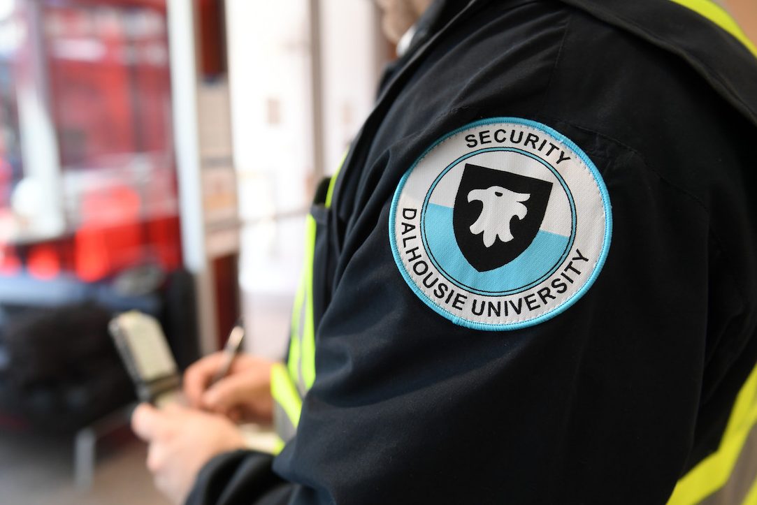 A guard wearing a badge that says "Dalhousie University Security" writes in a notepad. 