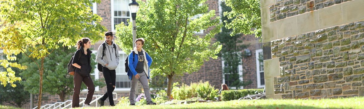 Three students walk across the Studley Quad with the Henry Hicks Building in the background.