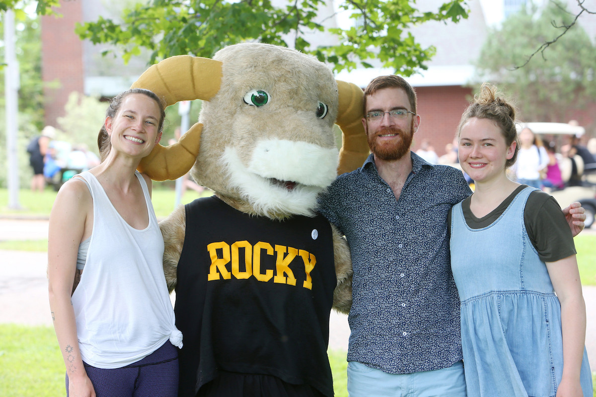 Ram mascot stands with arms around three people.