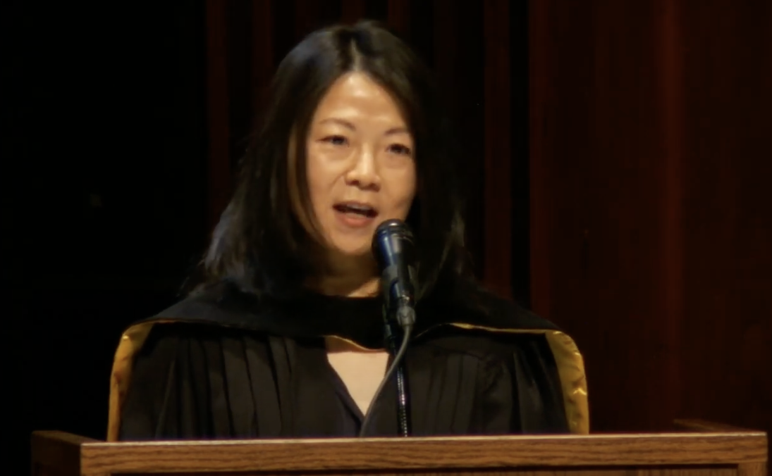 Person wearing academic dress speaks from lectern.