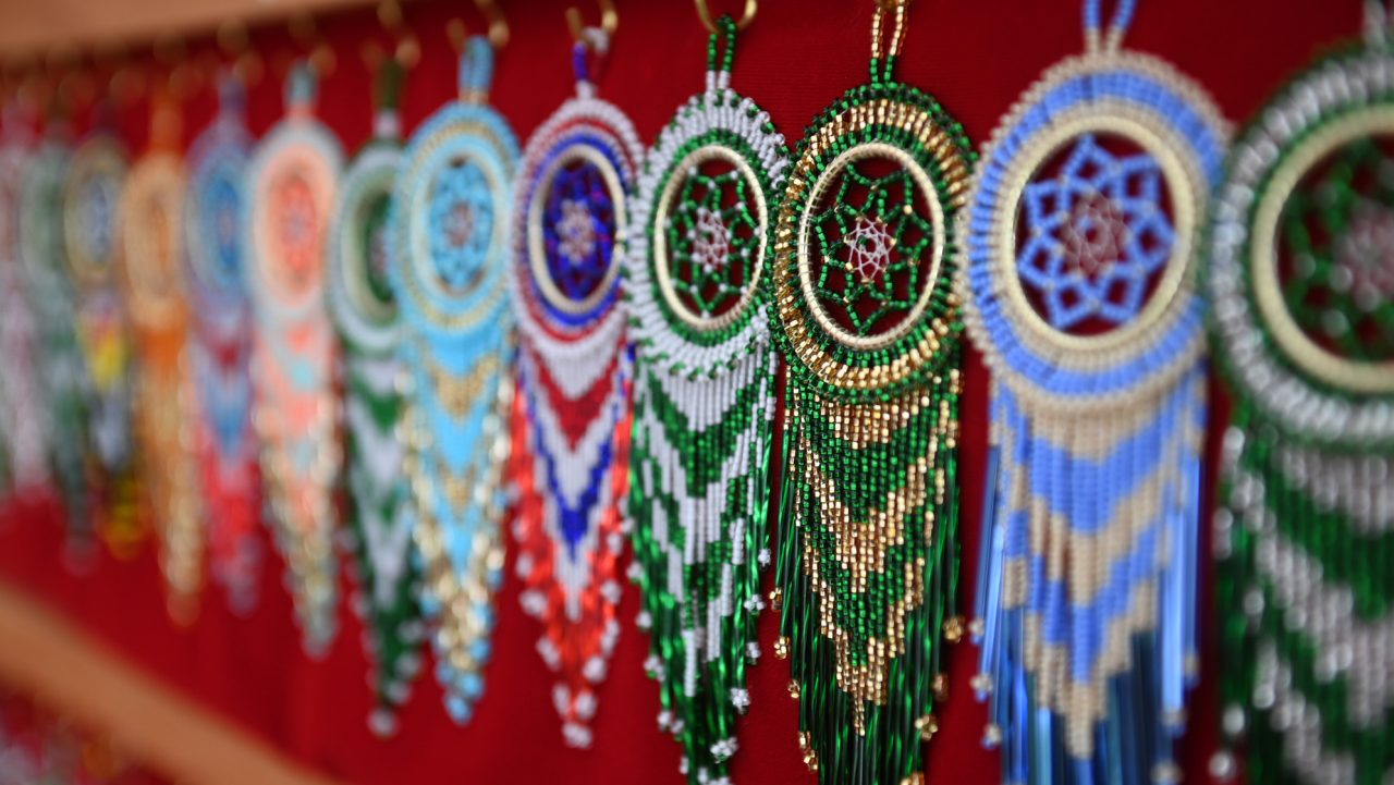A row of ornaments created from colourful beads hanging from hooks on a red background.