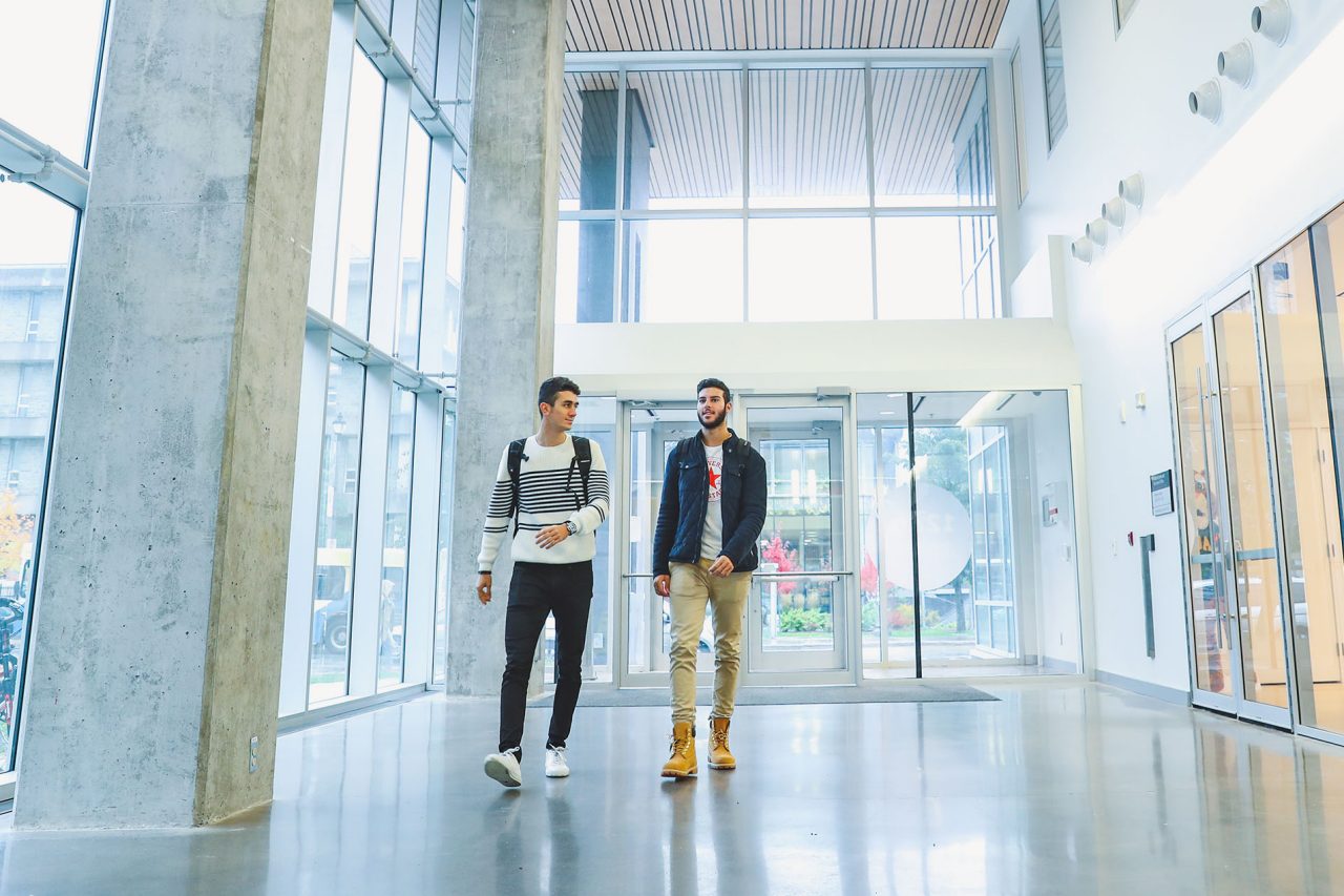 Two students walking along the brightly lit, windowed hall near the entrance of Dal's Health and Wellness Centre.