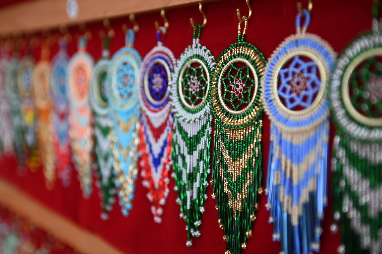 A row of ornaments created from colourful beads hanging from hooks on a red background.