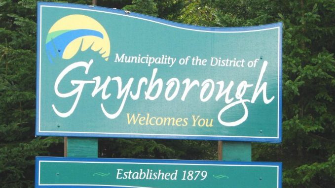 Green welcome sign for Guysborough with trees in the background