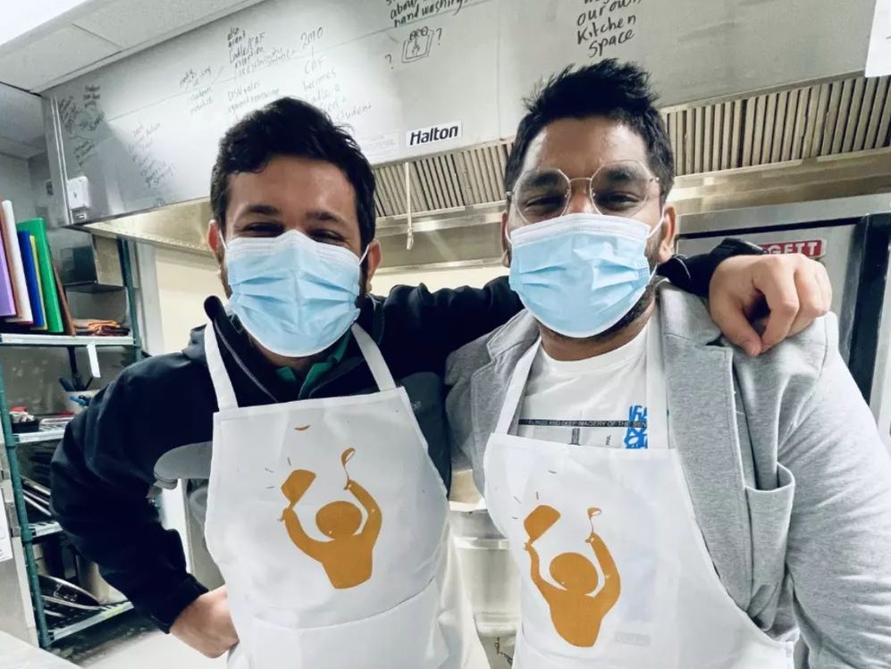 Two individuals wearing aprons standing in a commercial kitchen.