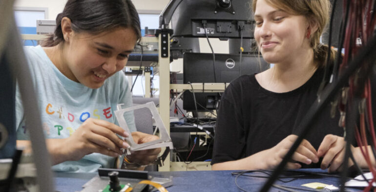 Two girls collaborating on electronics projects in a laboratory setting, focused on their work with various tools and components.