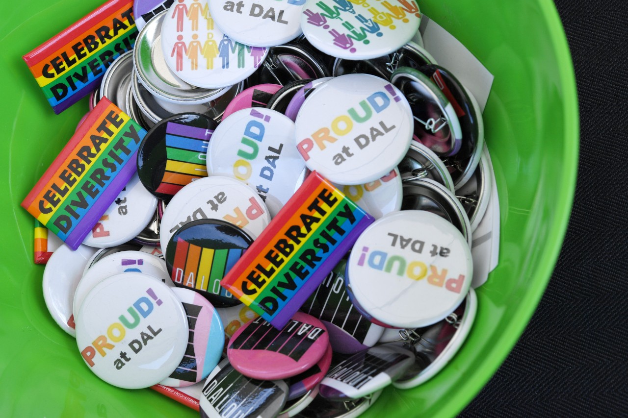 A collection of colourful pride buttons and pins in a green bowl.
