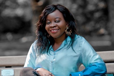 Temitayo Sodunke sits on a park bench wearing a blue silk shirt.