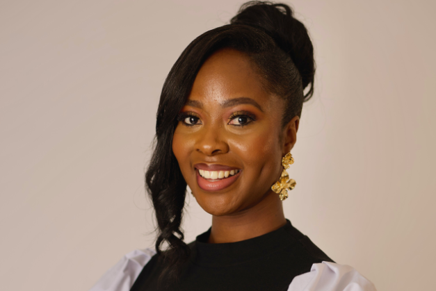 Karen Mutyabule smiles at the camera. She is wearing a black vest, white shirt, and gold earrings.