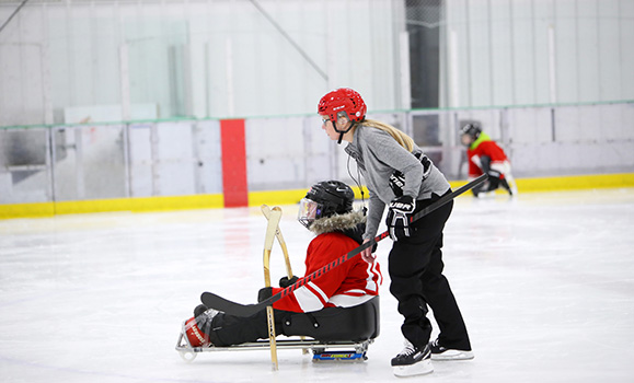 Student assists parasport hockey player on sled.