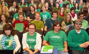Students sit in a lecture hall , many with green shirts.