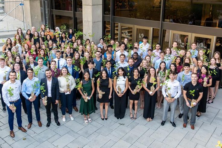 An aerial view of a group of approximately 70 students holding cherry trees.