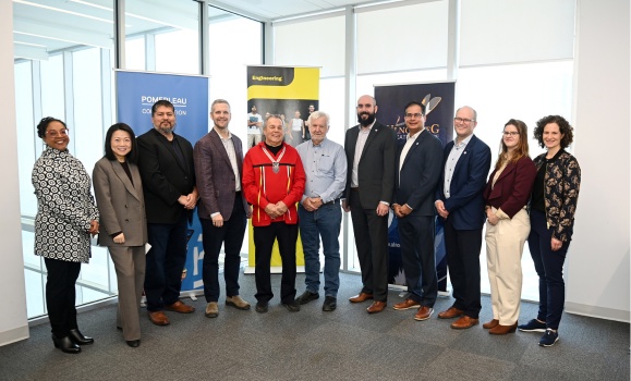 Eleven individuals are standing in a line in front of three organizational banners. 