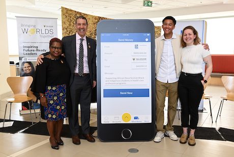 People gathered around a large image of a phone showing a screenshot of an RBC transaction from online banking.