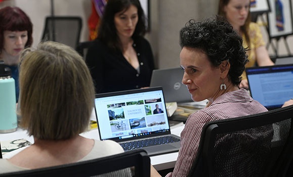 Five people are sitting at computers around a table with Wikipedia up on their screens.