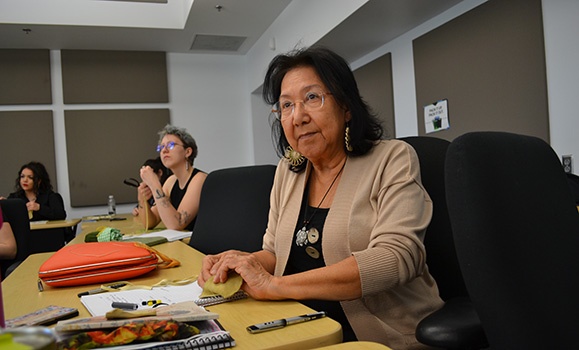Elder Ann and two students are sitting in black conference chairs around a table.
