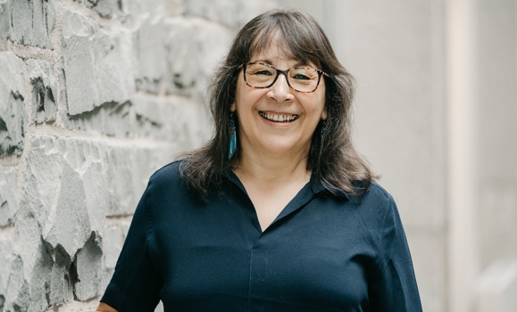 Dr. Sherry Pictou stands in front of a stone wall smiling at the camera.