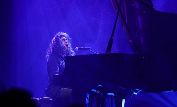Jeremy Dutcher is playing piano and singing into a microphone.