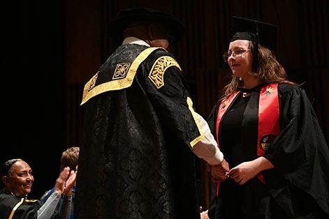 Kristan Belanger is on stage wearing the stole and a graduation cap.